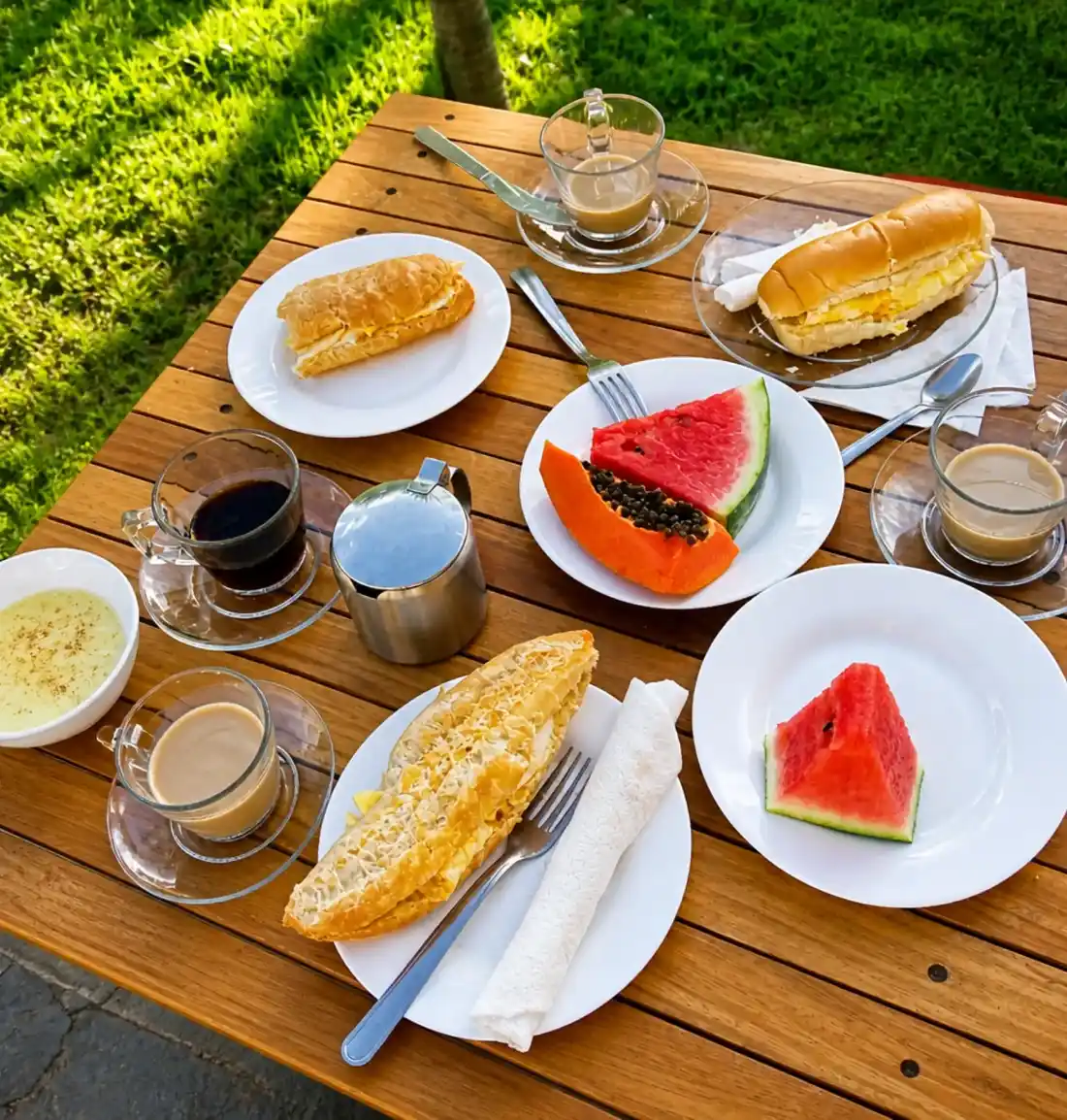 Café da manhã com café, frutas e pães em uma mesa ao ar livre